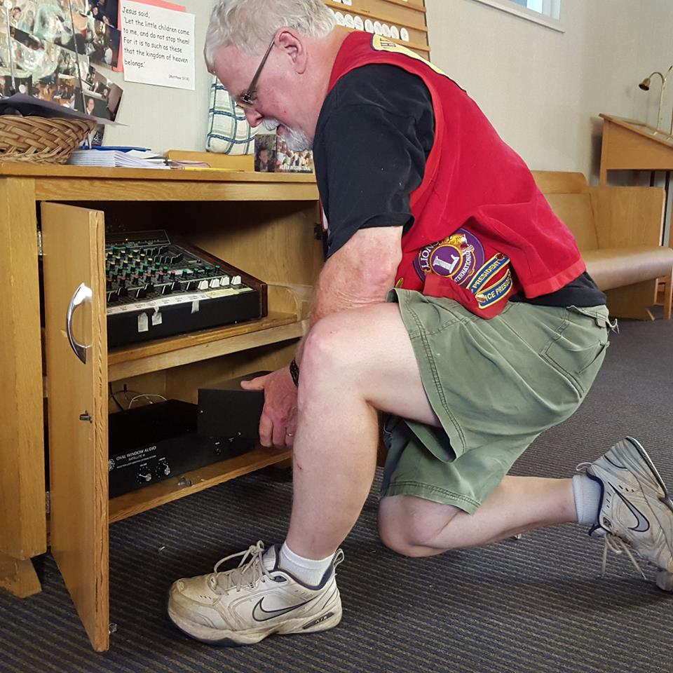 a man kneels in front of an equipment cabinet, sliding a device into it.